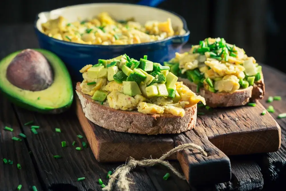 Scrambled eggs served over whole-grain toast and avocado.